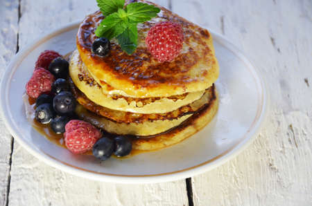Pancakes with berries and maple syrup in a plate on a white wooden background.の写真素材