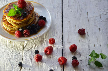 Pancakes with berries and maple syrup in a plate on a white wooden background.の写真素材