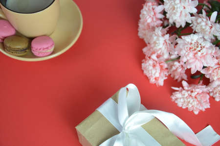 Mothers day or women's Day concept - box with a gift a beige cup of cappuccino beautiful white-pink aster flowers on a red background. good morning. greeting card. view from above. save space cookies macarune.の写真素材