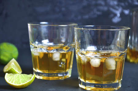 Drink cold tea with ice cubes and mint in two glass goblets a dark black background. Alcoholic or non-alcoholic mahito. whiskey or scotch tape, with lime or lemonの写真素材