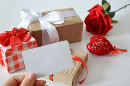 Girl holds a blank card without an inscription on the background of gifts with bows, ribbons and red rose on a white background. concept of discounts, gift, mothers day, womens day, valentines dayの写真素材