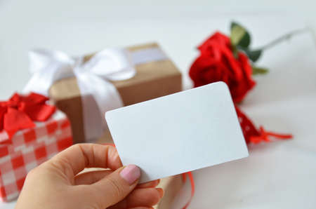 Girl holds a blank card without an inscription on the background of gifts with bows, ribbons and red rose on a white background. concept of discounts, gift, mothers day, womens day, valentines dayの写真素材