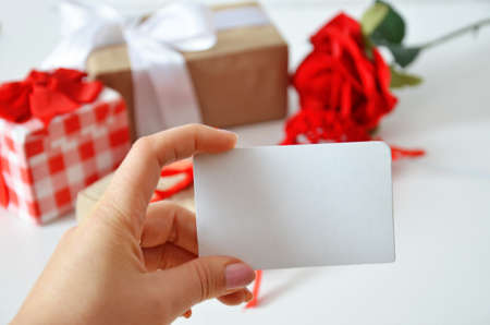 Girl holds a blank card without an inscription on the background of gifts with bows, ribbons and red rose on a white background. concept of discounts, gift, mothers day, womens day, valentines dayの写真素材