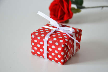 Homemade red present box with a gift tied with a ribbon, on a background a red rose on a white background, mothers day copy space of gifts for Christmas, valentines day, happy birthday, female hand.の写真素材