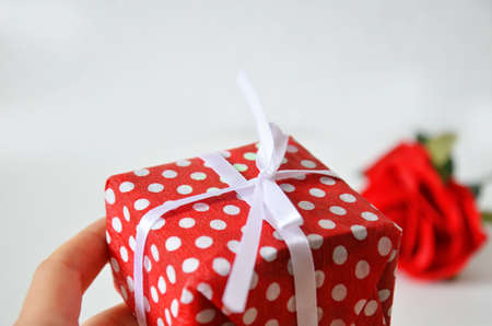 Homemade red present box with a gift tied with a ribbon, on a background a red rose on a white background, mothers day copy space of gifts for Christmas, valentines day, happy birthday, female handの写真素材