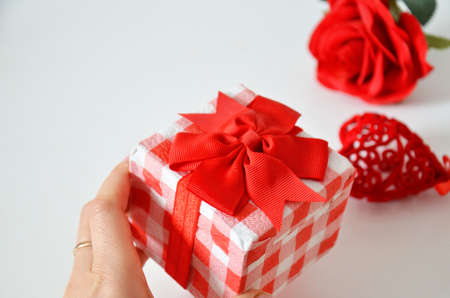 Homemade red present box with a gift tied with a ribbon, on a background a red rose on a white background, mothers day copy space of gifts for Christmas, valentines day, happy birthday, female handの写真素材