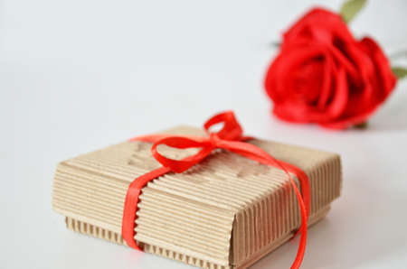 Homemade red present box with a gift tied with a ribbon, on a background a red rose on a white background, mothers day copy space of gifts for Christmas, valentines day, happy birthday, female handの写真素材