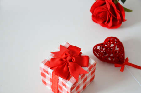 Homemade red present box with a gift tied with a ribbon, on a background a red rose on a white background, mothers day copy space of gifts for Christmas, valentines day, happy birthday, female handの写真素材