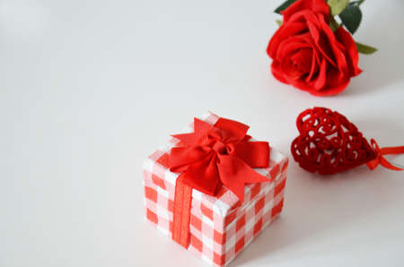 Homemade red present box with a gift tied with a ribbon, on a background a red rose on a white background, mothers day copy space of gifts for Christmas, valentines day, happy birthday, female handの写真素材
