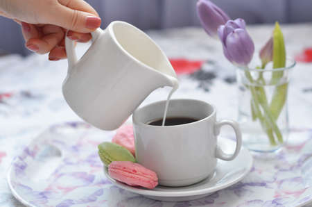 girl pour cream in coffee. Tray with paper sketchbook, smartphone and spring flowers on pink bedding. Relaxing, or working, or writing diary or blog in bed at home. with tablet.の写真素材