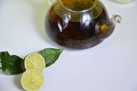 Transparent teapot with black tea, dry tea brewing on the table, bergamot slices, or lemon or lime on a white backgroundの写真素材