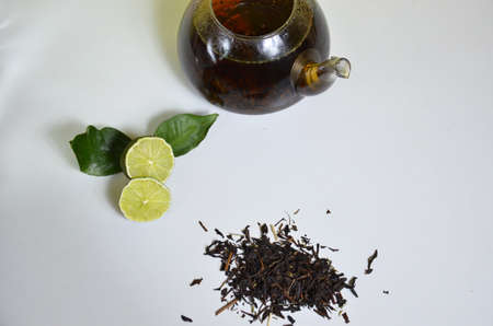 Transparent teapot with black tea, dry tea brewing on the table, bergamot slices, or lemon or lime on a white backgroundの写真素材
