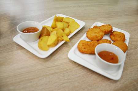 chicken nuggets and fried potatoes on a white plate on a table in a cafe or restaurant.の写真素材