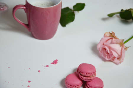 Three multicolored almond macaroons and a yellow mug with coffee on a white wooden background next to a pale pink rose. good morning concept.の写真素材