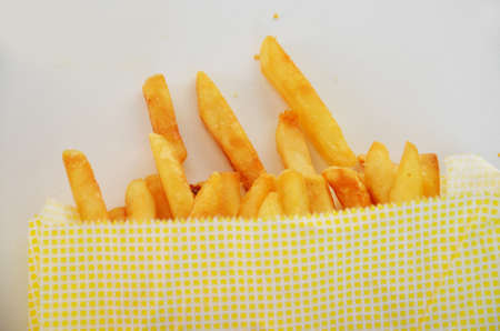 Serving of fries take takeaway. Girl takes french fries from the package on a white background in a paper bag.の写真素材