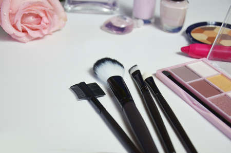 make-up brushes in holder and cosmetics isolated on white. lipstick, eye shadow, pink nail polish and pink roseの写真素材