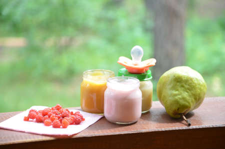 Baby food in jars puree mashed food on a background of foliage, With a pear banana, a pacifier and a spoonの写真素材