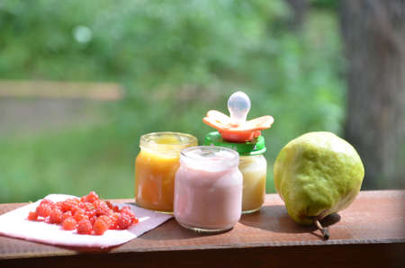 Baby food in jars puree mashed food on a background of foliage, With a pear banana, a pacifier and a spoonの写真素材