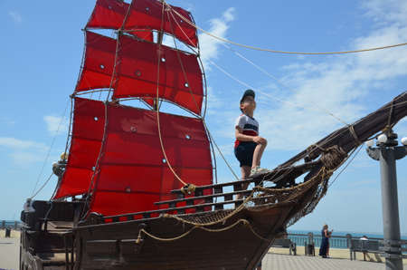 boy looks into the distance on an old ship with red sails. boy under the red sail.の写真素材
