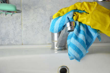 Housewife cleaning bathroom tap and shower Tap. Maid in yellow protective gloves washing dirty bath tap. Hands of woman washing or cleaning up bathの写真素材