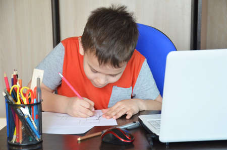 Smart Young Boy Works on a Laptop For His New Project in His Computer Science Class. Pupil doing homework at the computer at home. writes on paper. tired. sleeping on the table.の写真素材