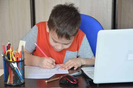 Smart Young Boy Works on a Laptop For His New Project in His Computer Science Class. Pupil doing homework at the computer at home. writes on paper. tired. sleeping on the table.の写真素材