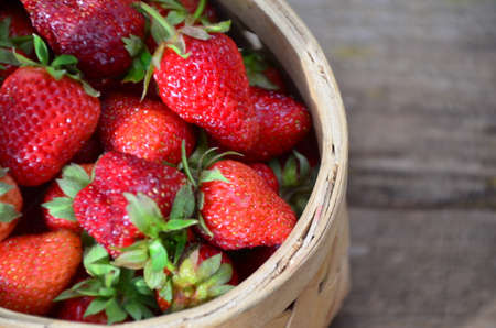 Ripe strawberries with leaves in wicker basket on wooden table on blurred backgroundの写真素材