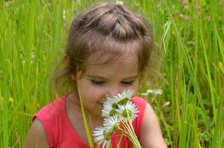 outdoor portrait Cute smiling baby girl in camomile field .Adorable girl with blue eyes and flowers daisies on meadow at summer day.Little child having fun and exploring nature. Copy spaceの写真素材