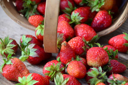 Ripe strawberries with leaves in wicker basket on wooden table on blurred backgroundの写真素材