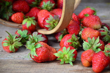 Ripe strawberries with leaves in wicker basket on wooden table on blurred background.の写真素材