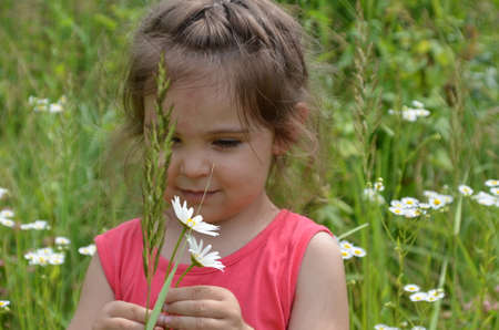 outdoor portrait Cute smiling baby girl in camomile field .Adorable girl with blue eyes and flowers daisies on meadow at summer day.Little child having fun and exploring nature. Copy spaceの写真素材