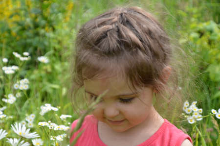 outdoor portrait Cute smiling baby girl in camomile field .Adorable girl with blue eyes and flowers daisies on meadow at summer day.Little child having fun and exploring nature. Copy spaceの写真素材