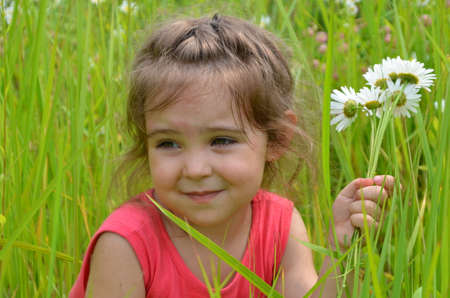 outdoor portrait Cute smiling baby girl in camomile field .Adorable girl with blue eyes and flowers daisies on meadow at summer day.Little child having fun and exploring nature. Copy spaceの写真素材