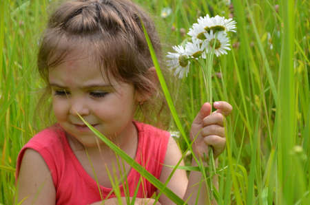 outdoor portrait Cute smiling baby girl in camomile field .Adorable girl with blue eyes and flowers daisies on meadow at summer day.Little child having fun and exploring nature. Copy spaceの写真素材