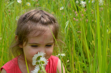 outdoor portrait Cute smiling baby girl in camomile field .Adorable girl with blue eyes and flowers daisies on meadow at summer day.Little child having fun and exploring nature. Copy spaceの写真素材