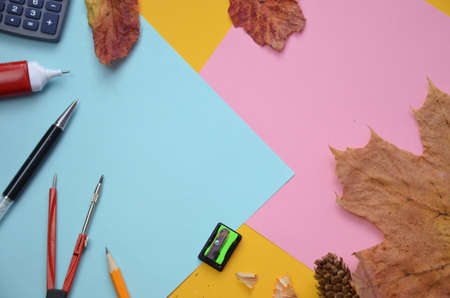 School office supplies with copy space. Back to school text concept. inscription flattering back to school on a colorful bright abstract background, calculator, autumn leaves, compasses, pencil, sharpener. Top viewの写真素材