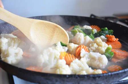 Mixed fresh vegetables in a skillet, fried stewed vegetables in a pan with a wooden spoon, broccoli, cauliflower and carrot vegetable stew, vegetarian, diet, few caloriesの写真素材