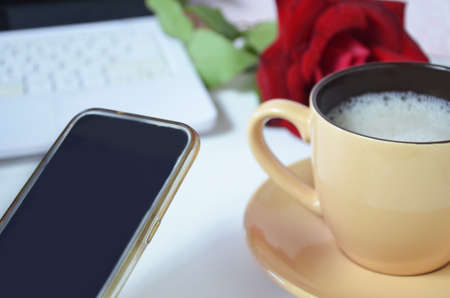 background of a cup with a coffee cappuccino mock up and a laptop on the desktop, red rose shot of...