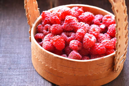 Fresh ripe raspberries in the wicker basket on wooden tableの写真素材