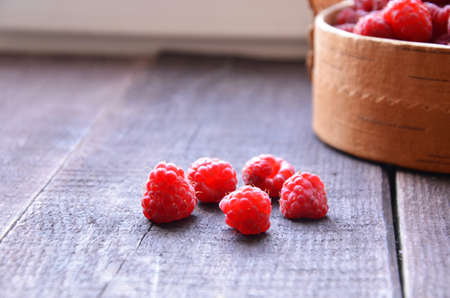 Fresh ripe raspberries in the wicker basket on wooden tableの写真素材