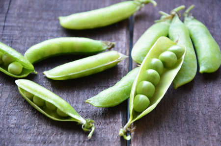 fresh green peas, just harvest. close up view of opened pod. spring vegetable up view on the wooden backgroundの写真素材