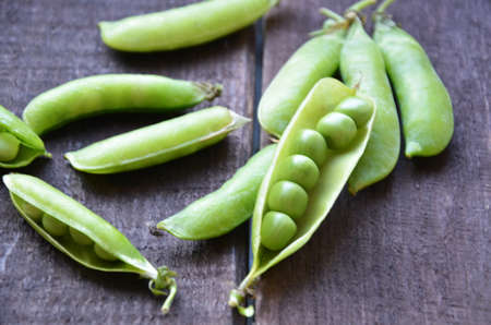 fresh green peas, just harvest. close up view of opened pod. spring vegetable up view on the wooden backgroundの写真素材