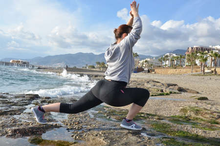 Beautiful blond girl clothing in at the seaside on the rock doing yoga poses, stretching or sports gymnastics and meditating in yoga pose.の写真素材