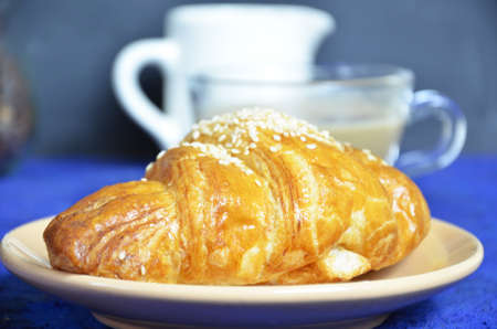 A plate with croissant cup of black with milk coffee and. Top View. The croissant is decorated with sesame. Complement the composition of a coffee beans and milk jug. healthy breakfast. good morning.の写真素材