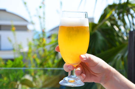 Hand holding a glass of beer in beach tropical sea background. vacation holiday conceptの写真素材