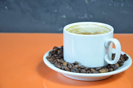 warm cup of coffee cappuccino with cream in a white cup on an orange and black background with coffee beans with a teaspoonの写真素材