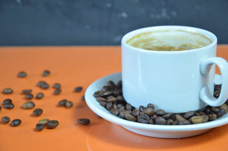 warm cup of coffee cappuccino with cream in a white cup on an orange and black background with coffee beans with a teaspoonの写真素材