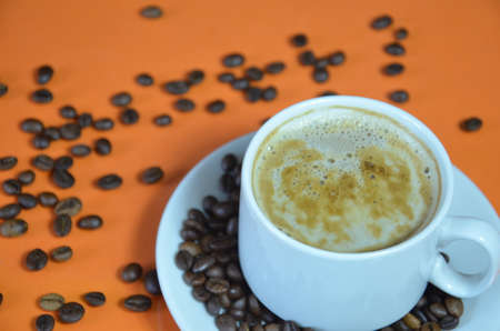 warm cup of coffee cappuccino with cream in a white cup on an orange and black background with coffee beans with a teaspoonの写真素材
