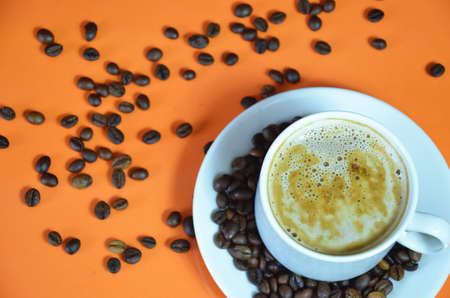 warm cup of coffee cappuccino with cream in a white cup on an orange and black background with coffee beans with a teaspoonの写真素材