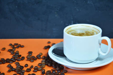warm cup of coffee cappuccino with cream in a white cup on an orange and black background with coffee beans with a teaspoonの写真素材